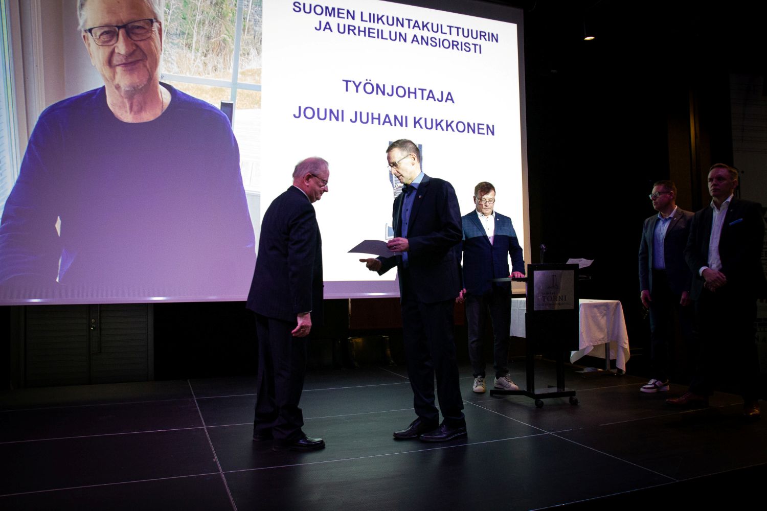 Miehelle annetaan ansioristi juhlatilaisuudessa.